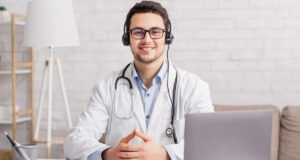 Health blog. Young doctor in headphones sitting at table with laptop