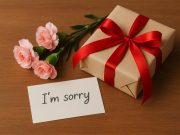 Beautifully wrapped gift box with a handwritten apology note and fresh flowers on a table